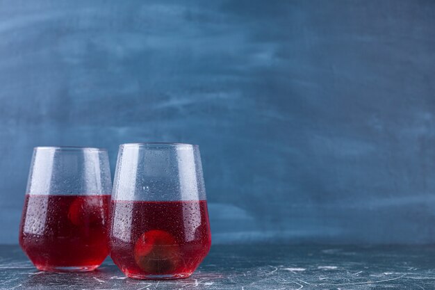 Two glass cups of fresh juice placed on a colorful background . 