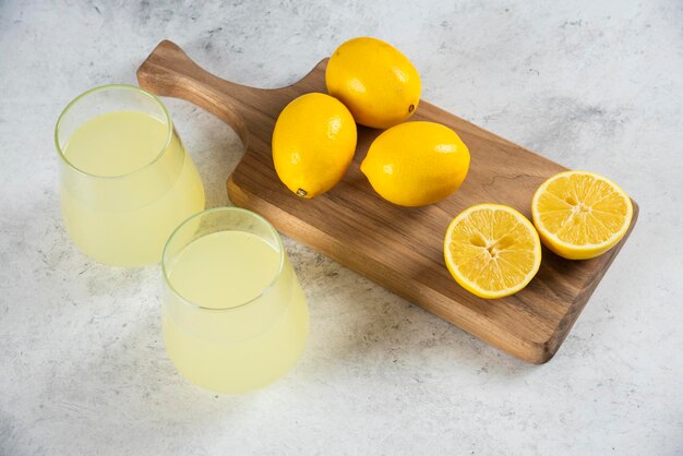 Two glass cups of fresh lemonade on a wooden board.