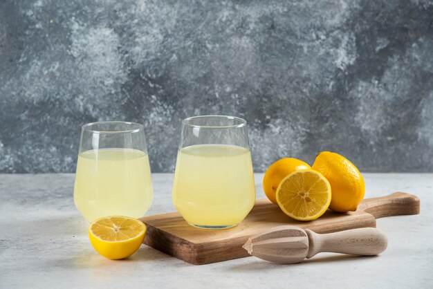 Two glass cups of fresh lemonade on a wooden board.