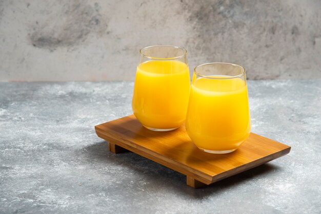 Two glass cups of fresh orange juice on wooden board.