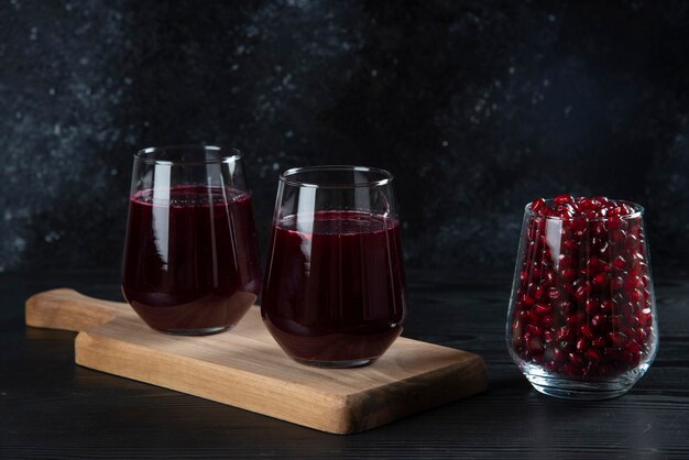 Two glass cups of fresh pomegranate juice on wooden board. 