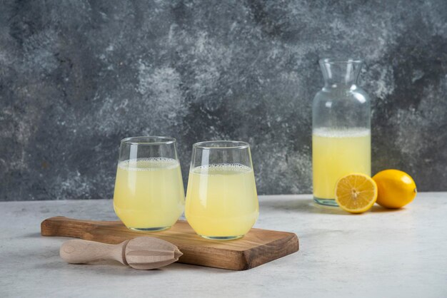 Two glass cups of lemonade on a wooden board.