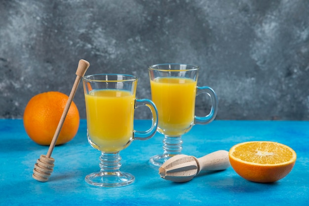 Two glass cups of orange juice with wooden reamer.