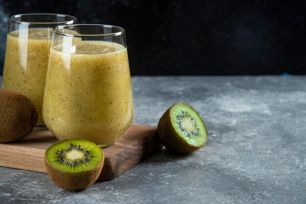 Two glass cups of tasty kiwi juice on wooden board. 