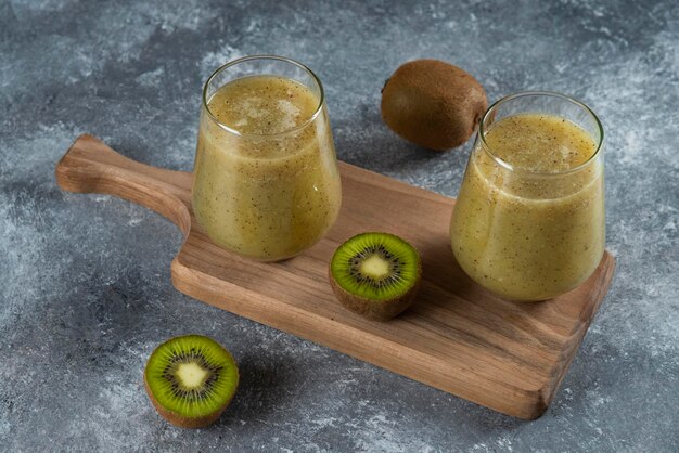 Two glass cups of tasty kiwi juice on wooden board. 