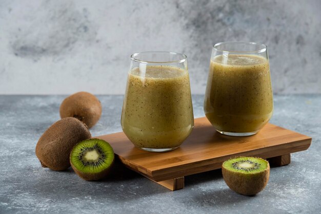 Two glass cups of tasty kiwi juice on wooden board. 