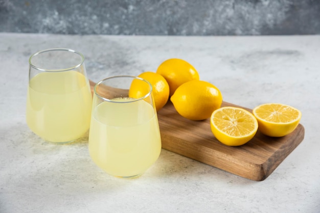 Two glass cups of tasty lemonade on a wooden board.