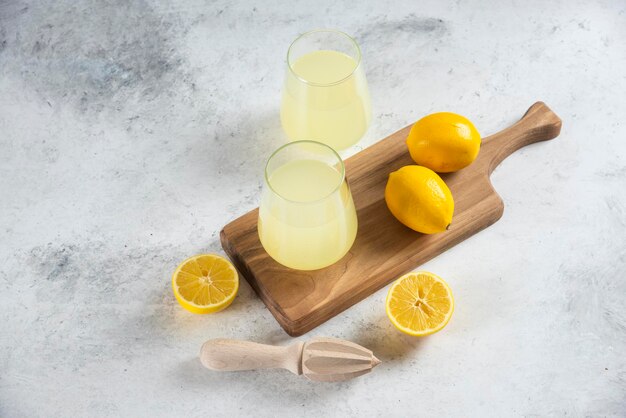 Two glass cups of tasty lemonade on a wooden board.