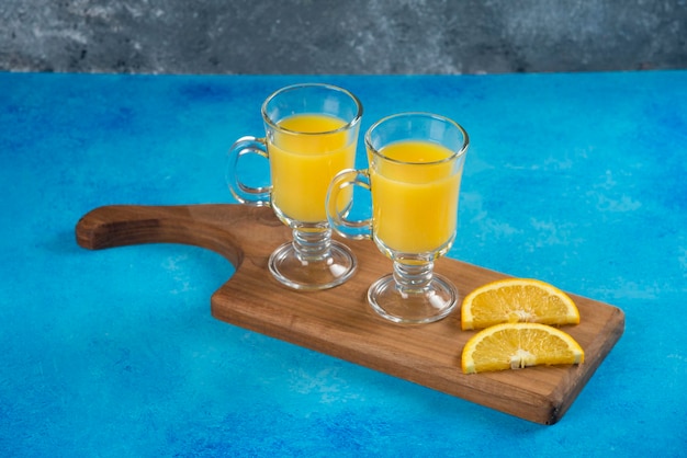 Two glass cups of tasty orange juice on wooden board.