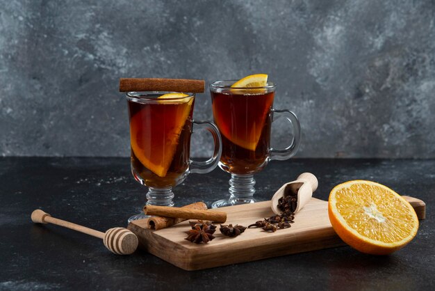 Two glass cups of tea and with cinnamon sticks and wooden dipper.