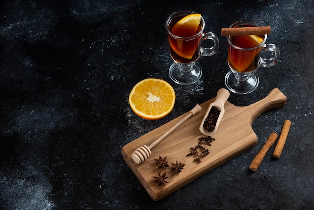 Two glass cups of tea and with cinnamon sticks and wooden dipper.