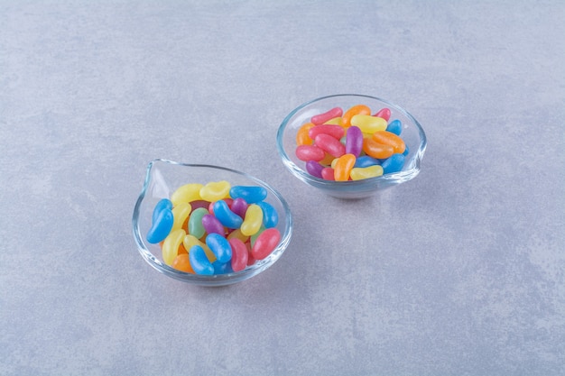 Две стеклянные тарелки с фруктовыми сладкими бобовыми конфетами на сине-серой поверхности