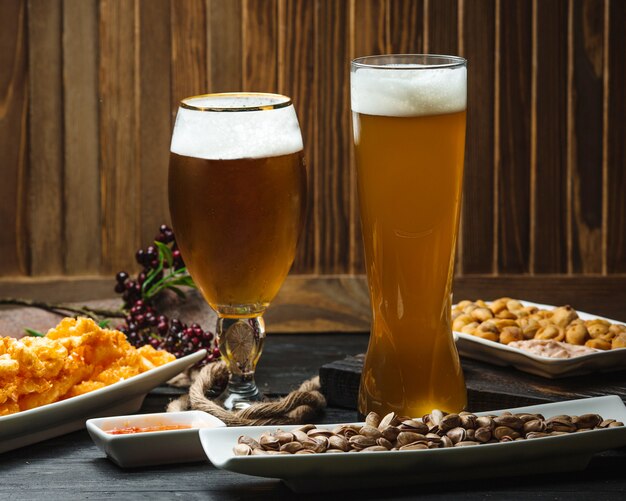 Два бокала пива подаются с фисташками, наггетсами и сладким соусом чили