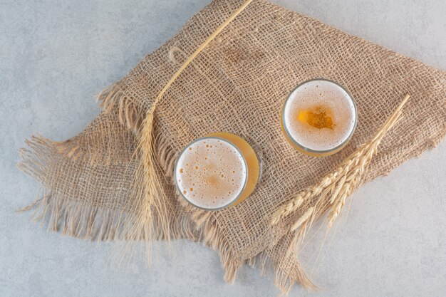 Two glasses of beer with wheat on sackcloth .