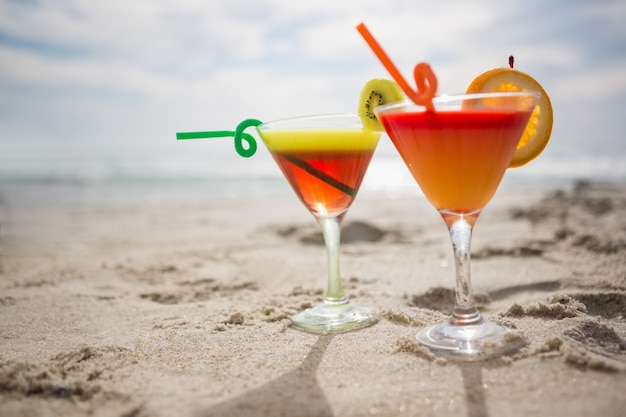 Два бокала коктейль держали на песке