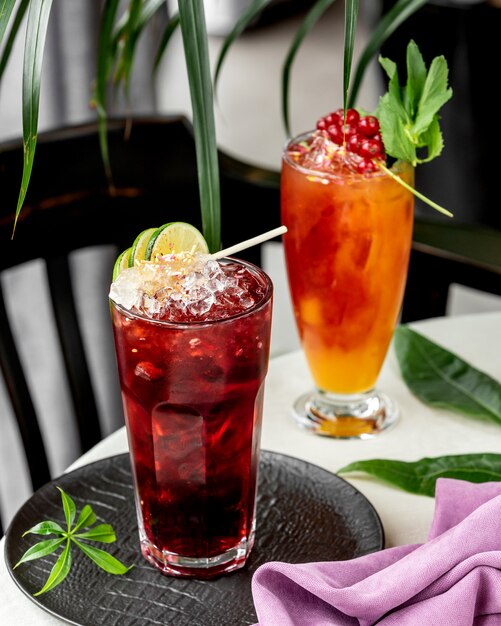 Two glasses of cocktails garnished with lime and redcurrant