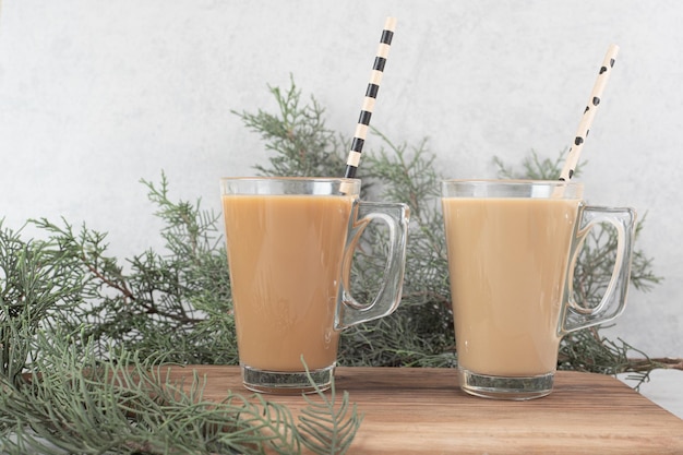 Two glasses of coffee with straws on wooden board