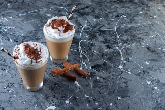 Two glasses of coffee with whipped cream on marble surface.