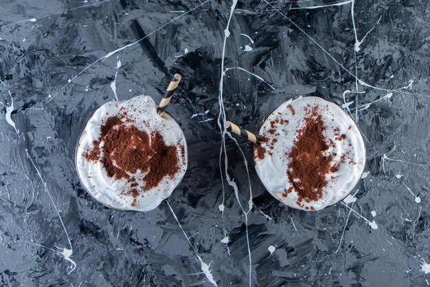 Two glasses of coffee with whipped cream on marble surface. 