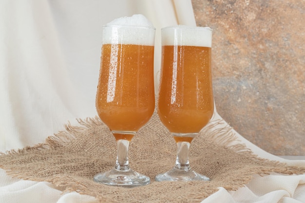 Two glasses of foamy beer on burlap