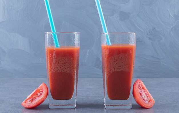 Due bicchieri di succo di pomodoro fresco e fette di pomodoro su uno sfondo grigio.