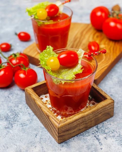 Two glasses of fresh tomato juice and tomatoes on gray concrete surface