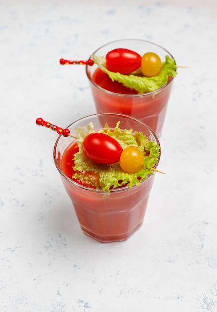 Two glasses of fresh tomato juice and tomatoes on gray concrete surface