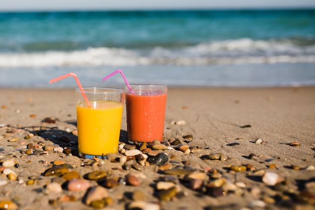 Two glasses of juice with drinking straw on sandy beach near the seashore