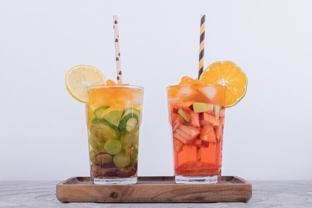Два стакана сока с кусочками фруктов на белой стене.