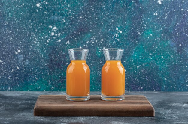 Two glasses of orange juice on wooden board.