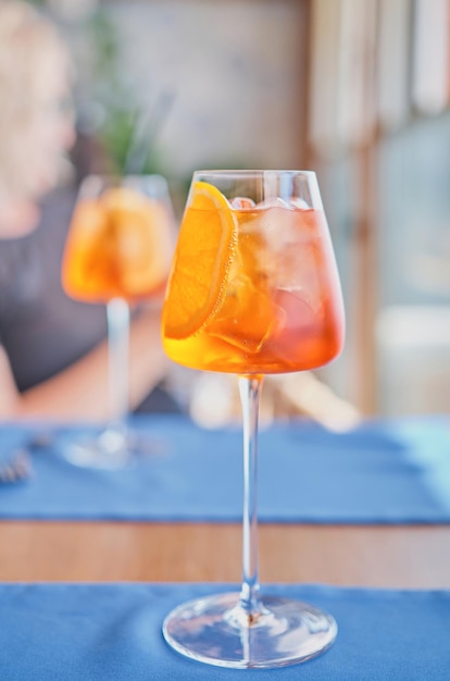 Free photo two glasses with colorful aperol spritz cocktail with ice on a dining table in a cafe blurred bright background selective focus of a weekend at sea refreshing drink