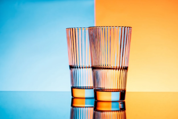 Foto gratuita due bicchieri di acqua su sfondo blu e arancio.