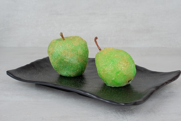 Foto gratuita due mele scintillanti sulla banda nera su superficie bianca.