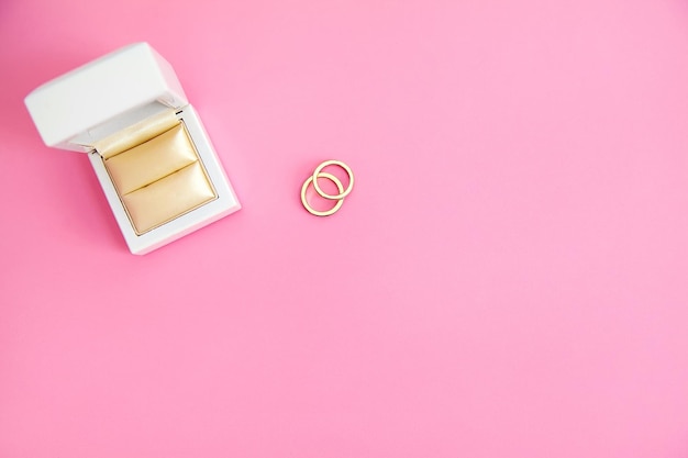 Two gold rings near white box on pink creame background