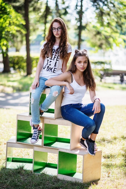 Two gorgeous young girls sitting on wooden boxes in the park on a sunny day