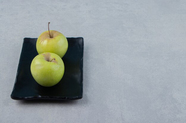 Two green apples on black plate