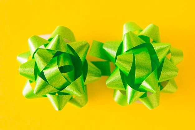 Two green satin ribbon bows on yellow background