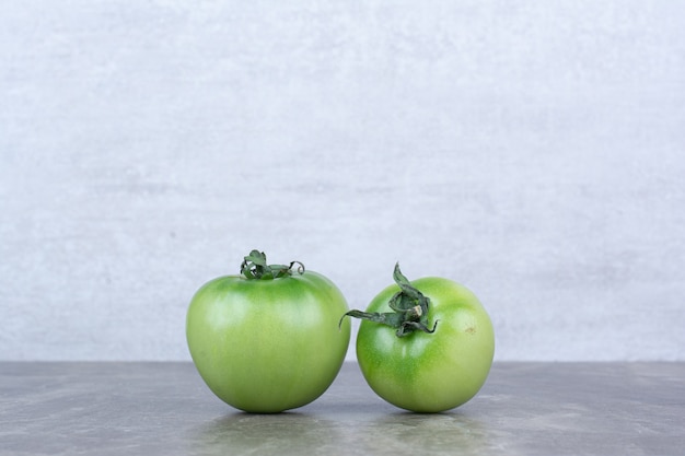 Two green tomatoes on marble table.