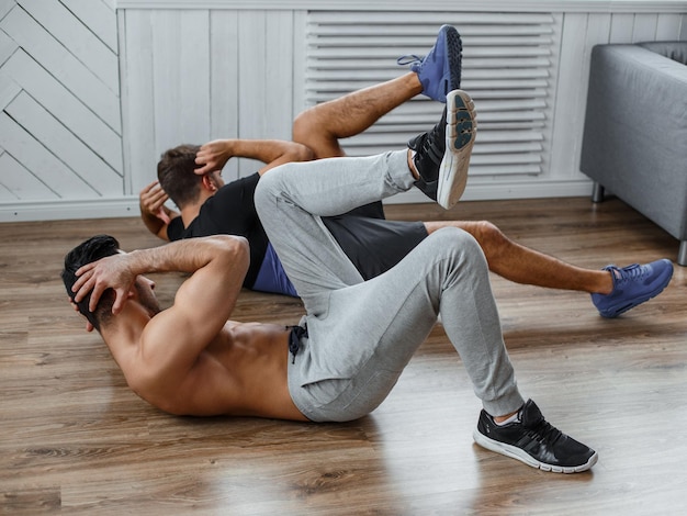 Two guys doing stomach workouts lying on the floor.