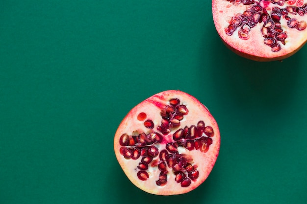 Two halved pomegranate on green background