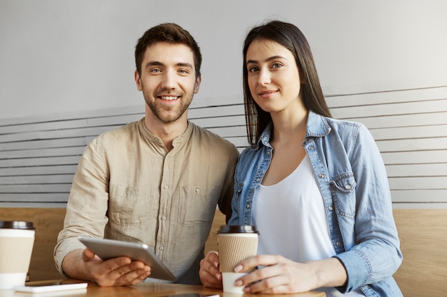 coworking 공간에 앉아 커피를 마시고 팀 프로젝트에 대해 얘기하는 두 잘 생긴 프리랜서. 남자와여자가 웃 고, 기사에 대 한 포즈.