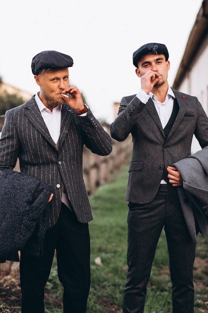 Free photo two handsome men in suit smoking at ranch
