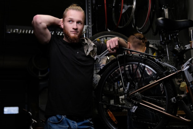 Два красивых стильных мужчины работают с велосипедом в ремонтной мастерской. Рабочие ремонтируют и монтируют велосипед в мастерской.