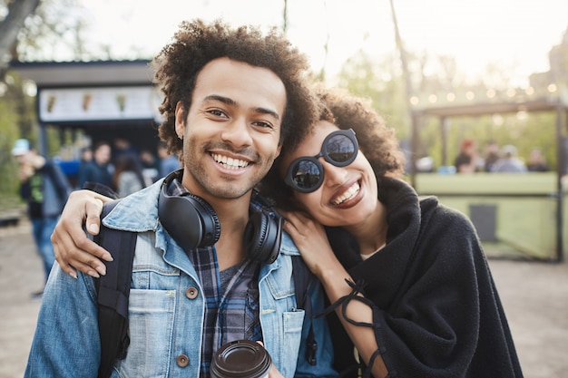 아프로 헤어 스타일 포옹과 카메라를보고, 공원에서 산책하는 동안 사진을 만들고, 긍정적 인 감정을 표현하는 두 명의 행복한 아프리카 계 미국인 여행자.