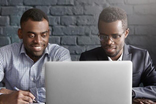 Two happy African colleagues using laptop