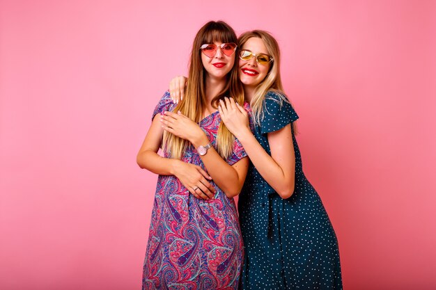 Two happy best friends sister women girls wearing trendy spring summer printed bright vintage dresses and sunglasses 