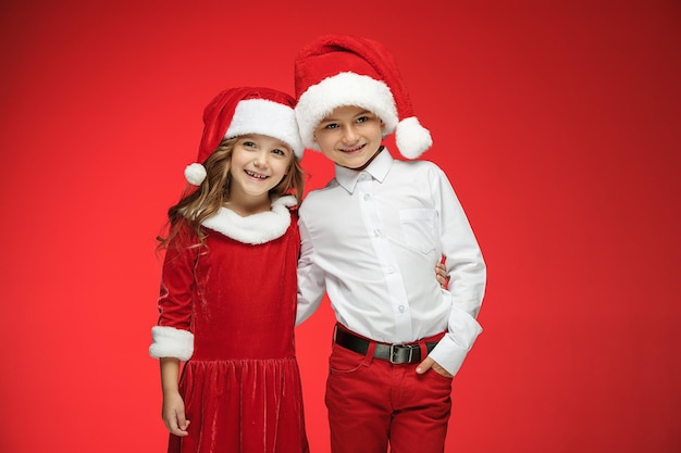 Due ragazzo e ragazza felici in cappelli di babbo natale con scatole regalo in studio rosso