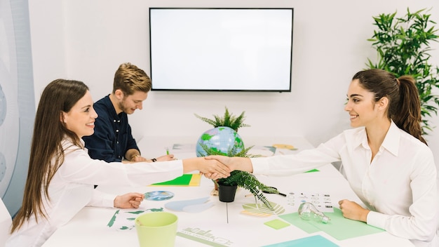 Two happy businesswomen shaking hands over desk