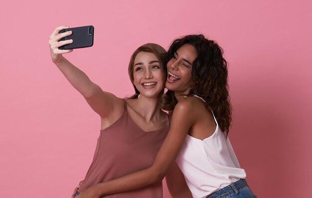 Two happy carefree teenage girl taking selfie looking at smartphone front camera