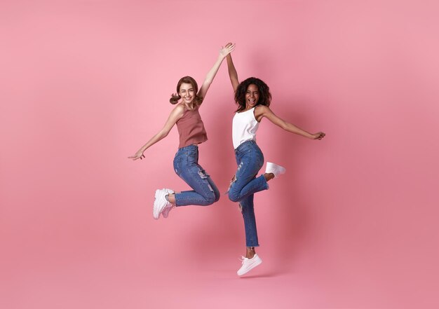 분홍색 배경 위로 점프하는 두 명의 행복한 평온한 젊은 여성